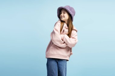 Gülümseyen küçük bir kızın portresi şık bir şapka takıyor ve kollarını kavuşturup mavi arka planda poz veriyor. Reklam kavramı