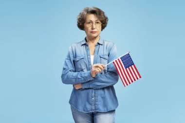 Amerikan bayrağı taşıyan ciddi kendinden emin yaşlı bir kadının portresi Bağımsızlık Günü 'nü mavi arka planda izole etti. Seçim, özgürlük kavramı 