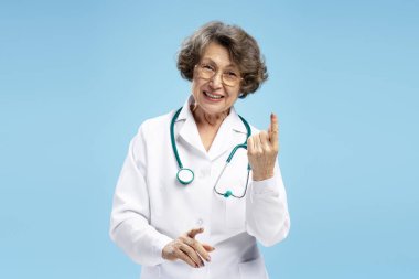 Gülümseyen güzel yaşlı kadın portresi, beyaz önlüklü doktor, steteskop, mavi arka planda izole edilmiş kameraya bakan. Sağlık hizmeti kavramı