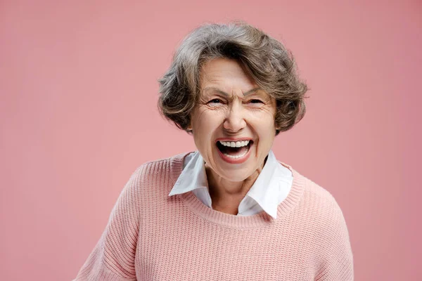 Portrait of smiling beautiful senior gray haired woman wearing casual clothes laughing looking at camera isolated on pink background. Advertisement concept, dental care