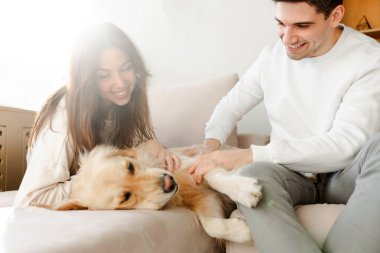 Mutlu gülümseyen genç bir çiftin portresi, sevgili ve sevgili evcil köpek, rahat bir kanepede uzanan Golden retriever rahat bir ev rahatlaması. Hayvan bakımı konsepti