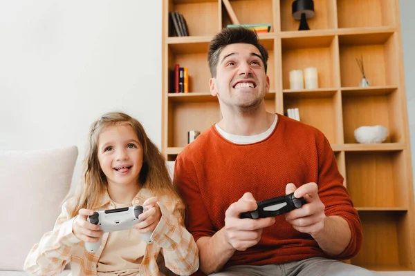 Gülümseyen, yakışıklı bir adam ve kızının video oyunları oynayıp, elinde joystick tutarak rahat bir odada oturduğu portre. Çevrimiçi teknoloji kavramı