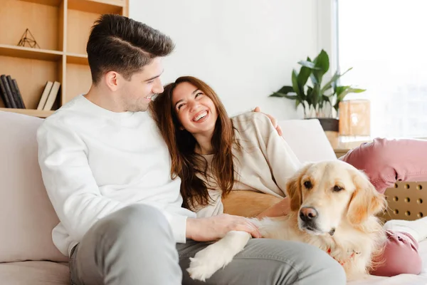 魅力的な笑顔の若いカップル ボーイフレンドとガールフレンドの肖像画は 居心地の良い家で快適なソファーに座って犬を抱きしめます 愛の概念 動物の世話 — ストック写真