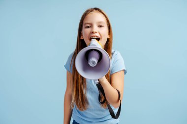 Portrait of smiling beautiful girl wearing casual clothes holding loudspeaker, announcing something isolated on blue background. Advertisement concept clipart