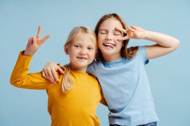 Gülümseyen kızların portresi, mavi arka planda izole edilmiş kameraya bakan şirin kız kardeşler. Stüdyoda poz veren genç mutlu mankenler. Çocukluk, pozitif yaşam tarzı konsepti 