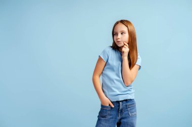Güzel, şık, küçük bir kızın portresi. Mavi arka planda yalnız poz veriyor. Moda konsepti 