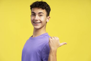 Sarı arka planda izole edilmiş fotokopi alanındaki kameraya bakan sıradan mor tişörtlü gülümseyen yakışıklı çocuk portresi. Reklam kavramı