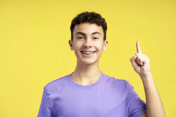 노란색 배경에 공간에 손가락을 보여주는 카메라를 캐주얼 보라색 티셔츠를 미소의 — 스톡 사진