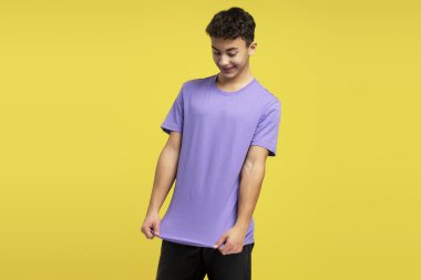 Yakışıklı, güler yüzlü, şık bir mor tişört giyen, ona bakan, sarı arka planda tek başına duran adam. Alışveriş kavramı, depolama