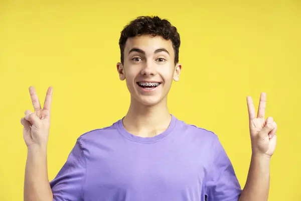 Smilende Tenåringsgutt Med Tannregulering Som Viser Seier Tegn Ser Kamera – stockfoto