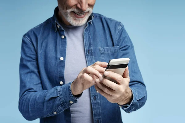 笑容满面的退休大胡子男人穿着时髦的衣服 手持智能手机手机应用 查看邮件 有选择的焦点 蓝色背景隔离的肖像 技术概念 — 图库照片