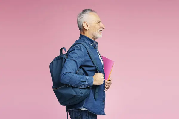 一个面带微笑的老人的侧视图画像 一个拿着背包的成熟的学生 还有那些被粉色背景隔开的书 教育概念 — 图库照片