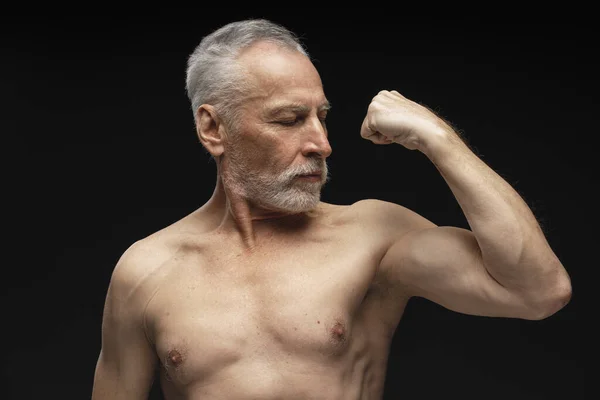 迷人而严肃的老年人的画像 运动员表现出二头肌 被黑色背景隔离的肌肉体 广告概念 — 图库照片
