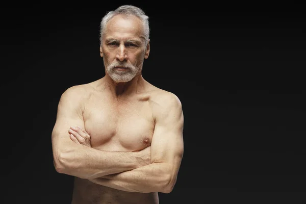 六十岁的英俊老年男子的画像 身披赤裸的躯干 双臂交叉地站在黑色背景上 凝视着相机 复制空间 健康生活方式概念 — 图库照片