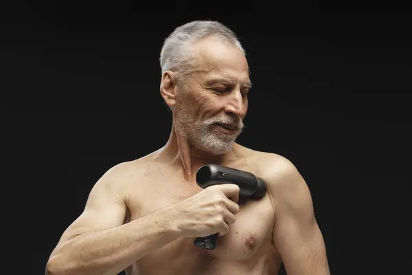 英俊的老年人的画像 穿着无袖上衣 用按摩枪 站在黑色背景孤立 保健概念 — 图库照片