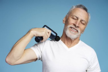 Yakışıklı, gülümseyen gri saçlı bir adamın portresi, beyaz tişörtlü, gözleri kapalı, mavi arka planda izole edilmiş boyun masajı yapan bir emeklinin portresi. Sağlık ve tedavi kavramı