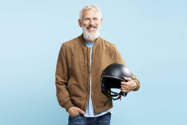Yakışıklı, güler yüzlü olgun bir adam, gri saçlı, sakallı motosikletli, mavi arka planda motosiklet kaskı takan. 