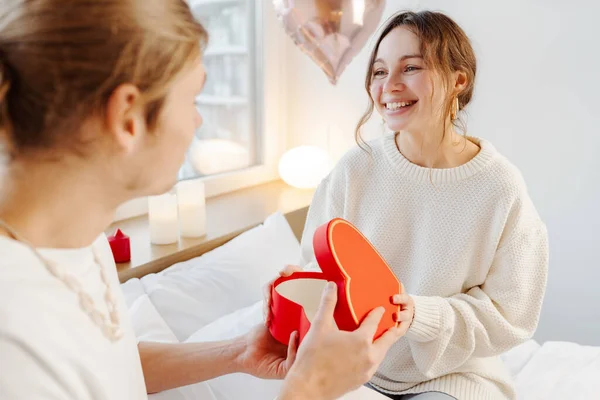 美しく 笑顔の女性が赤いギフト用の箱を開け 彼女のボーイフレンドからのプレゼントは 自宅の寝室に座っています バレンタインデーコンセプト — ストック写真