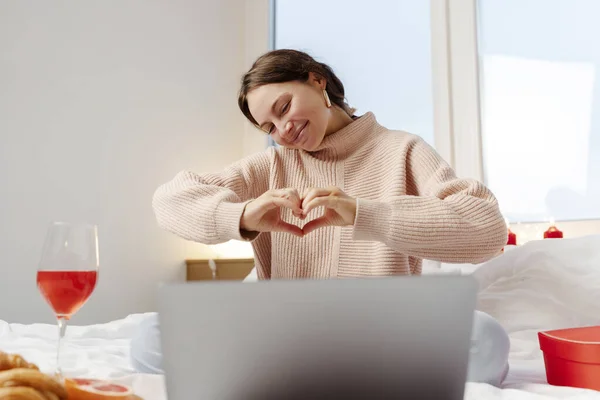 Pozytywna Kobieta Siedząca Mieszkaniu Pokazująca Serce Palcami Korzystająca Laptopa Mająca — Zdjęcie stockowe