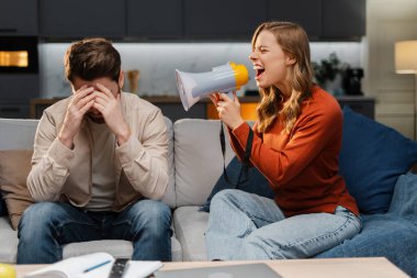 Kızgın genç bir kadının portresi, elinde megafon, adamla konuşuyor, evdeki kanepede otururken yüksek sesle bağırıyor. İlişki kavramı, kavga, çatışma