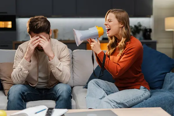 Kızgın genç bir kadının portresi, elinde megafon, adamla konuşuyor, evdeki kanepede otururken yüksek sesle bağırıyor. İlişki kavramı, kavga, çatışma