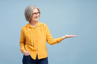 Mavi arka planda izole edilmiş fotokopi alanını gösteren kendinden emin gülümseyen son sınıf öğrencisi kadın portresi. Alışveriş, satış, reklam konsepti 