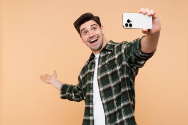 Mutlu, şaşkın adam, el hareketleriyle bej rengi arka planda izole edilmiş cep telefonundan kameraya bakıyor. 