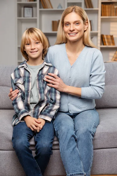 Inside their cozy living room, smiling mother and her son enjoy close embrace on couch, their joyful expressions and affectionate cuddle illustrating perfect picture of homebound happiness