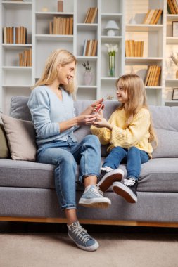 Rahat bir Anneler Günü kutlaması: Lüks bir koltukta oturan bir kız, annesini kalpten bir kartla şaşırtır, annesinin yüzünü aydınlatır.