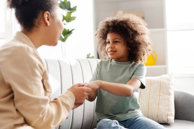 Afro-Amerikan bir anne ve kızının bir kanepede otururken sarmaş dolaş, gülümseme ve şefkatli bakışlarla neşeli bir sohbeti paylaştığı hoş bir yuva.