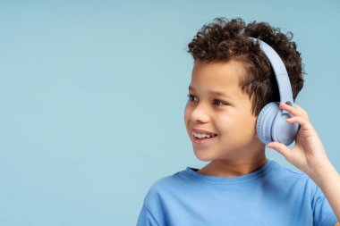 Gençlik tarzı koleksiyon resmi: Mavi tişörtlü gülümseyen Afro-Amerikalı çocuk, kablosuz kulaklık kullanıyor, mavi arka planda izole edilmiş neşeli bir ifadeyle titreşiyor.