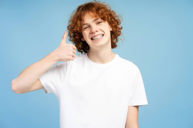 Sevdim, aferin. Diş teli takmış mutlu genç bir adamın tasvir edilmiş portresi başparmak hareketi yapıyor, onay işareti gösteriyor, mükemmel geri bildirim. Stüdyo içi çekim, mavi arkaplan 