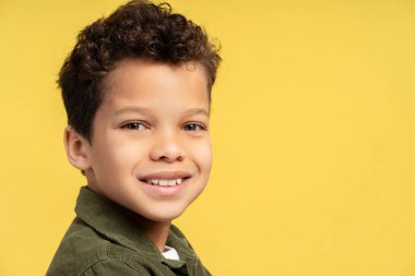 Gülümseyen, sıradan kıyafetler giyen, sarı arka planda izole edilmiş kameraya bakan, yakın çekim yapan yakışıklı Afro-Amerikan çocuk. Reklam kavramı