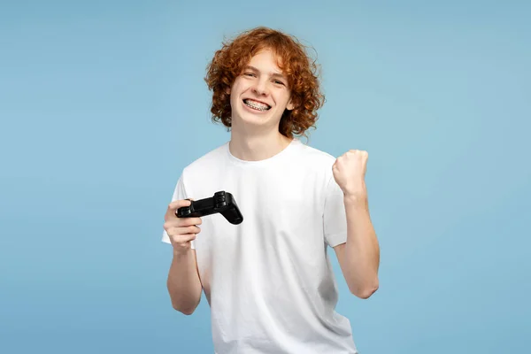 Smiler Krøllete Rødhårete Tenåring Mann Med Tannregulering Holder Spillkontroller Viser – stockfoto