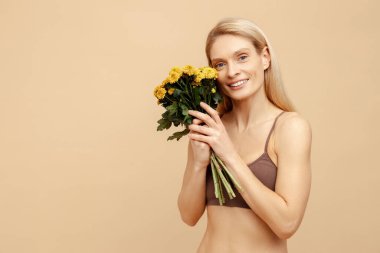 Portre gülümseyen orta yaşlı çekici bir kadın elinde bej arka planda izole edilmiş güzel bir buket bahar çiçeği tutuyor, fotokopi alanı. Doğal güzellik konsepti 