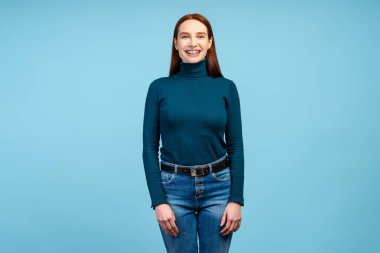 Mavi arka planda izole edilmiş kameraya bakan dişlerinde diş teli olan gülümseyen kendine güvenen kızıl kadının portresi. Sağlık, tedavi, ortodontik konsept