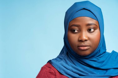 Yakın plan portresi. Mavi arka planda izole edilmiş tesettürlü, ciddi Müslüman kadın. Dindar Afrikalı öğrenci başka tarafa bakıyor, boşluğu kopyala. Eğitim kavramı