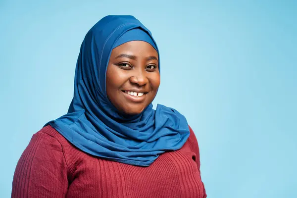 Portrait beautiful smiling muslim woman wearing traditional hijab isolated on blue background. Happy religious African American student looking at camera, education concept