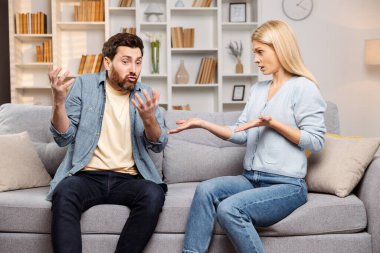 Ev içi çatışma sahnesi. Bir erkek ve bir kadın, bir tartışma sırasında el kol hareketi yapıyorlar. Oturma odasındaki kanepede birlikte oturuyoruz.