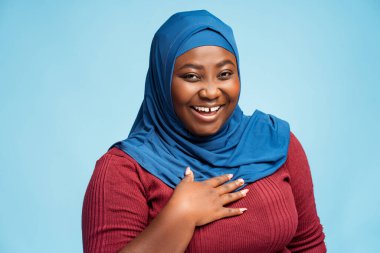 Mavi arka planda geleneksel tesettüre bürünmüş çekici gülümseyen Arap kadın portresi. Mutlu Afrikalı Afrikalı Amerikalı iş kadını kameraya bakıyor, iş konsepti