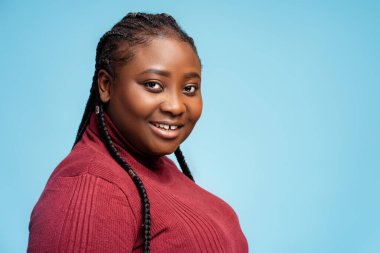 Mutlu, gülümseyen Afro-Amerikan kadın şık kırmızı süveter giyip kameraya bakıyor, mavi arka planda izole poz veriyor, fotokopi çekiyor. Reklam konsepti, moda