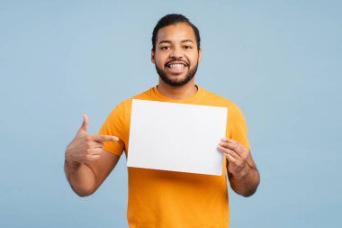 Yüzünde diş teli olan gülümseyen Afro-Amerikan bir adamın portre fotoğrafı, boş bir poster sunuyor ve ona doğru parmağıyla işaret ediyor, kameraya bakıyor, mavi bir arkaplanda izole edilmiş. Model konsepti