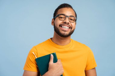 Gözlüklü, gülümseyen Afro-Amerikan adam mavi arka planda izole edilmiş kitaplar tutuyor. Mutlu öğrenci çalışıyor, kameraya bakarak dil öğreniyor. Eğitim kavramı 