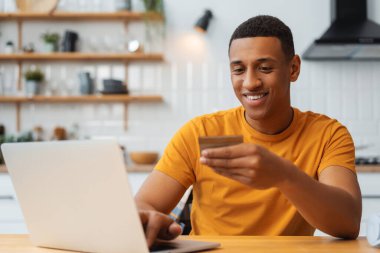 Kredi kartı tutan, dizüstü bilgisayar kullanan, seçen, ödeme yapan, online alışveriş yapan çekici bir Afrikalı Amerikalı. İndirimde satın alan yakışıklı bir adam. Çevrimiçi bankacılık kavramı