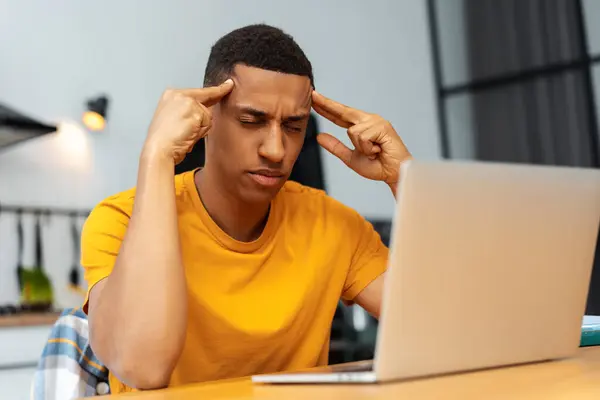 Portrait of tired, upset African American man touching head, using laptop, eyes closed, having headache, stress, migraine, depression. Treatment concept