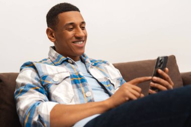 Gülümseyen yakışıklı Afro-Amerikan adam, cep telefonu tutan iş adamı rahat koltukta oturan, sipariş veren, online alışveriş yapan mobil uygulama kullanıyor. Sosyal medya ve teknoloji kavramı