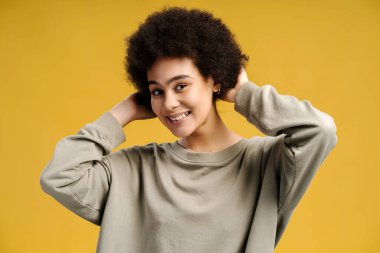 Mutlu otantik Afrikalı Amerikalı kadın, kıvırcık saçlı manken sarı arka planda izole edilmiş kameraya bakıyor. Saç bakımı konsepti, tedavi