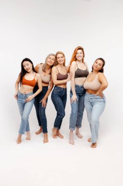 Güzel, çekici kadınlardan oluşan bir grup seksi sutyen ve kot pantolon giyip kameraya bakıyor. Gülümseyen moda kadınları sarı arka planda izole bir şekilde duruyorlar. Uluslararası Kadınlar Günü konsepti