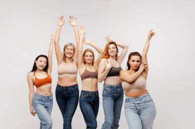 Kendine güvenen, seksi sutyenler giyen, beyaz arka planda izole edilmiş şık kotlar giyen çok kültürlü kadınlar. Moda modelleri stüdyoda kameraya bakıyor. Çeşitlilik, Uluslararası Kadınlar Günü