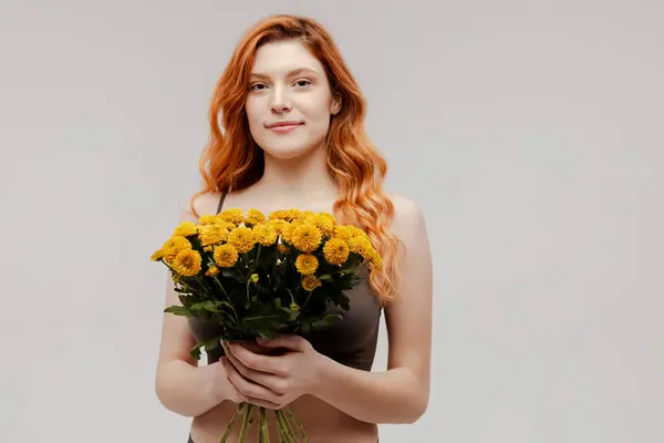 Portrait of cheerful young ginger woman wearing stylish underwear holding bouquet of beautiful flowers isolated on white background. Natural beauty, spring, International women\'s day concept